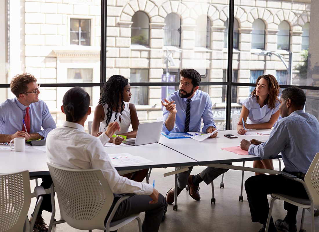 Business Insurance - Group of Business Professionals Having a Discussion While Sitting Around a Table in a Bright Conference Room During a Business Meeting