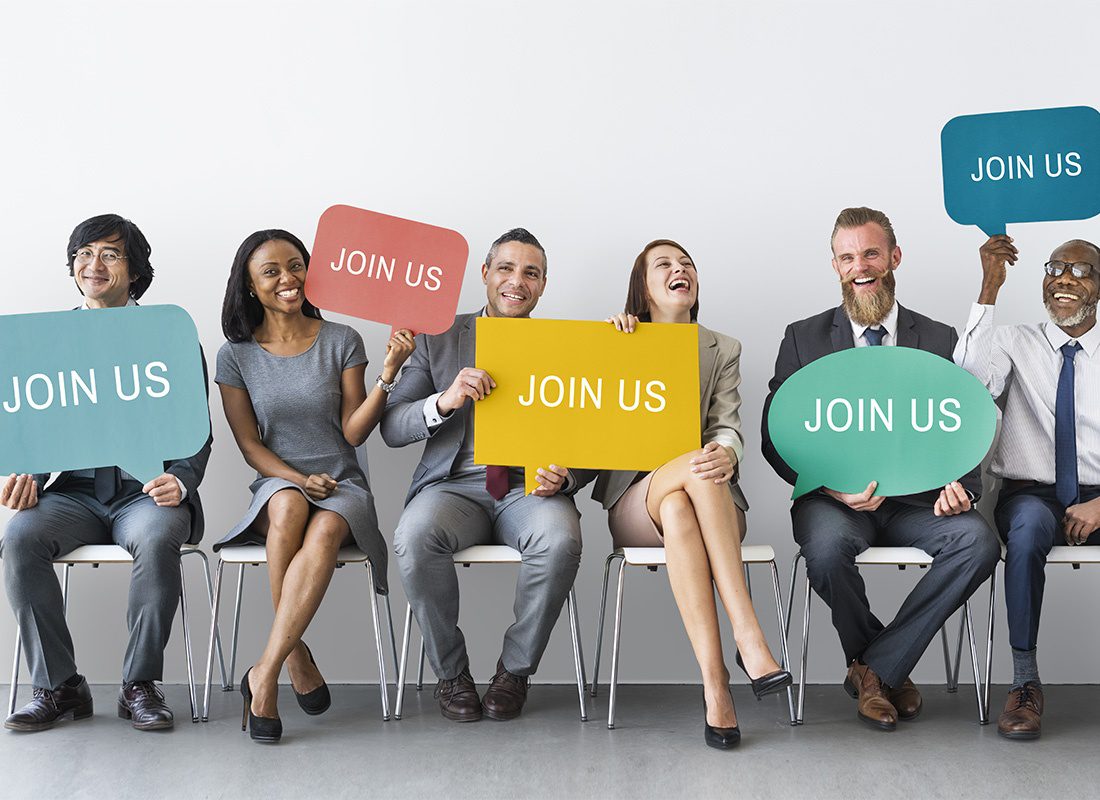 Careers - Cheerful Group of Diverse Business People Sitting in Chairs While Holding Up Colorful Join Us Signs