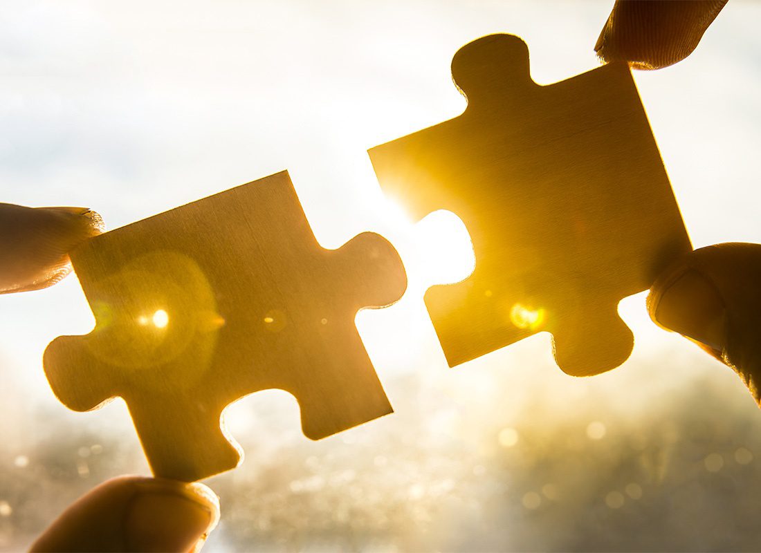 Claims Advocacy - Closeup View of a Man's Fingers Holding Up Two Puzzle Pieces Against a Bright Sunny Sky