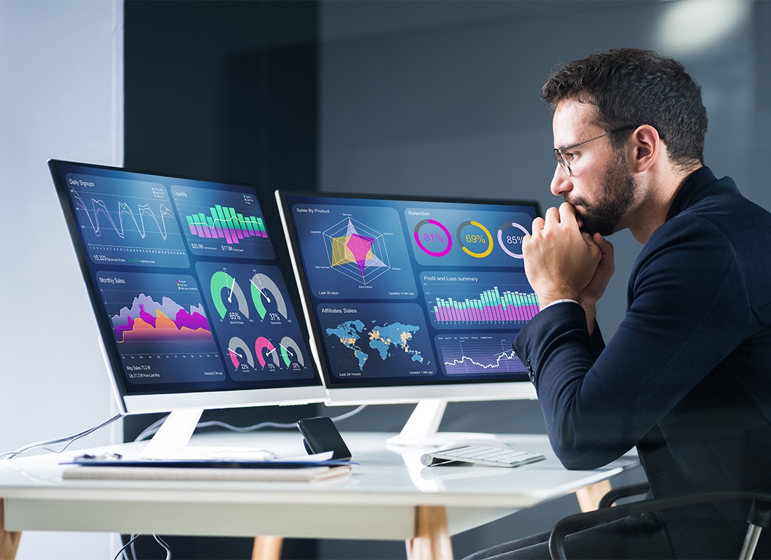 Modeling and Analytics - Portrait of a Young Business Man Looking at Two Monitor Screens with Analytics and Statistics Charts While Sitting in the Office